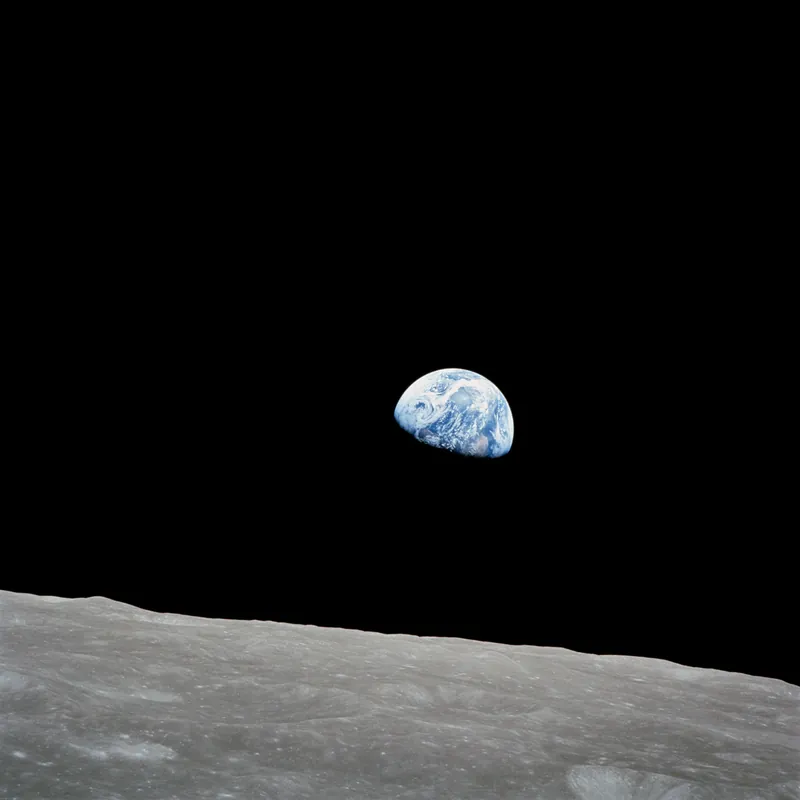Pământul răsărind deasupra orizontului cenușiu al Lunii, pe jumătate luminat de Soare, fotografiat de pe orbita lunară